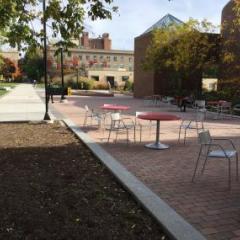 Outdoor tables and chairs on pavement near a tree lined walkway with buildings in the background at Cornell University